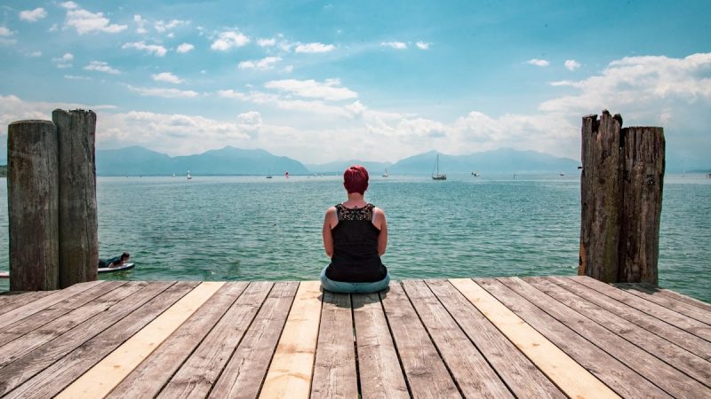 man in red t-shirt sitting on wooden dock during daytime